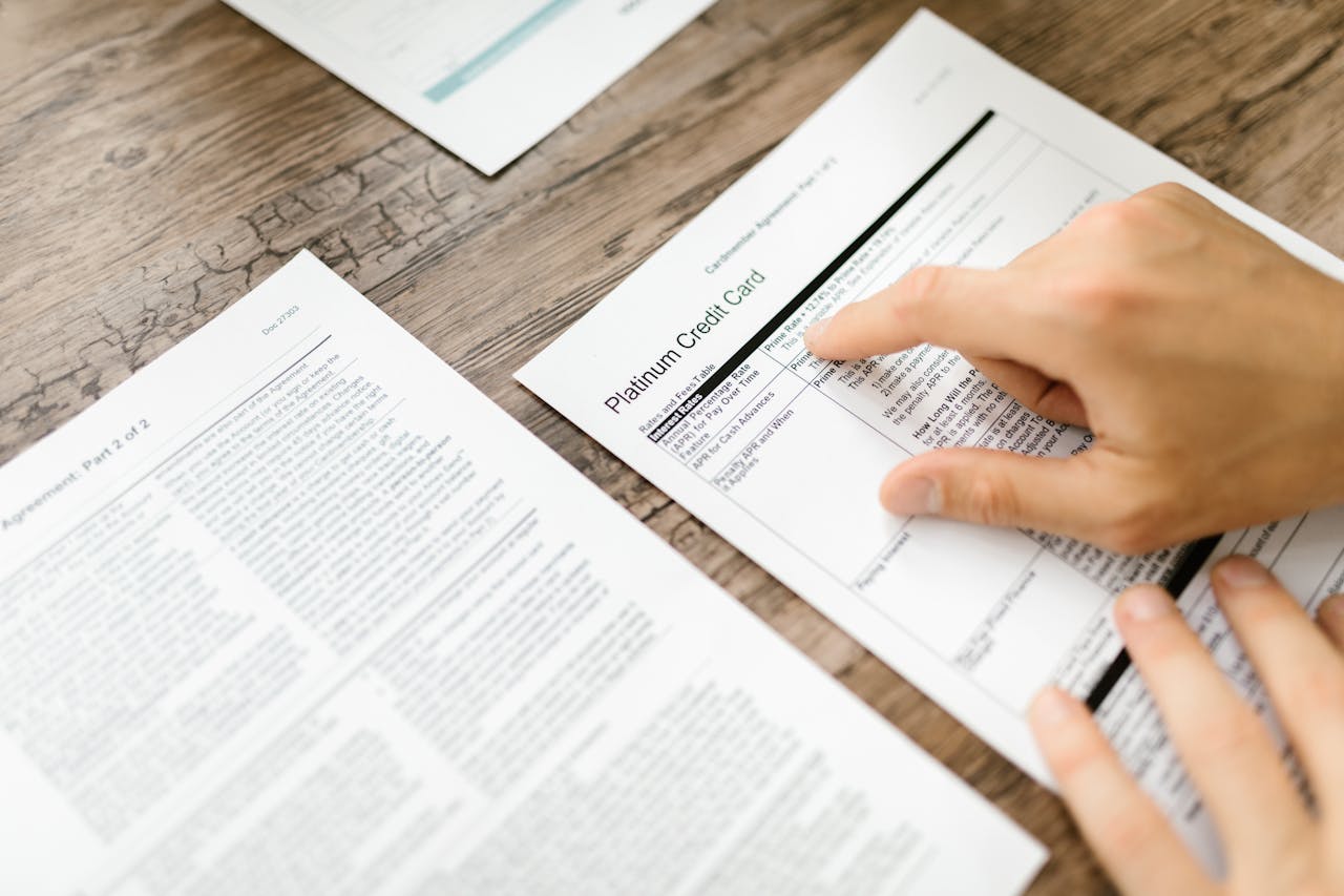 Home A hand examining a credit card agreement on a wooden desk, highlighting financial review.